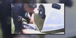 Police bodycam footage displaying an officer rescuing a resident lying on the grass next to a white patrol car.