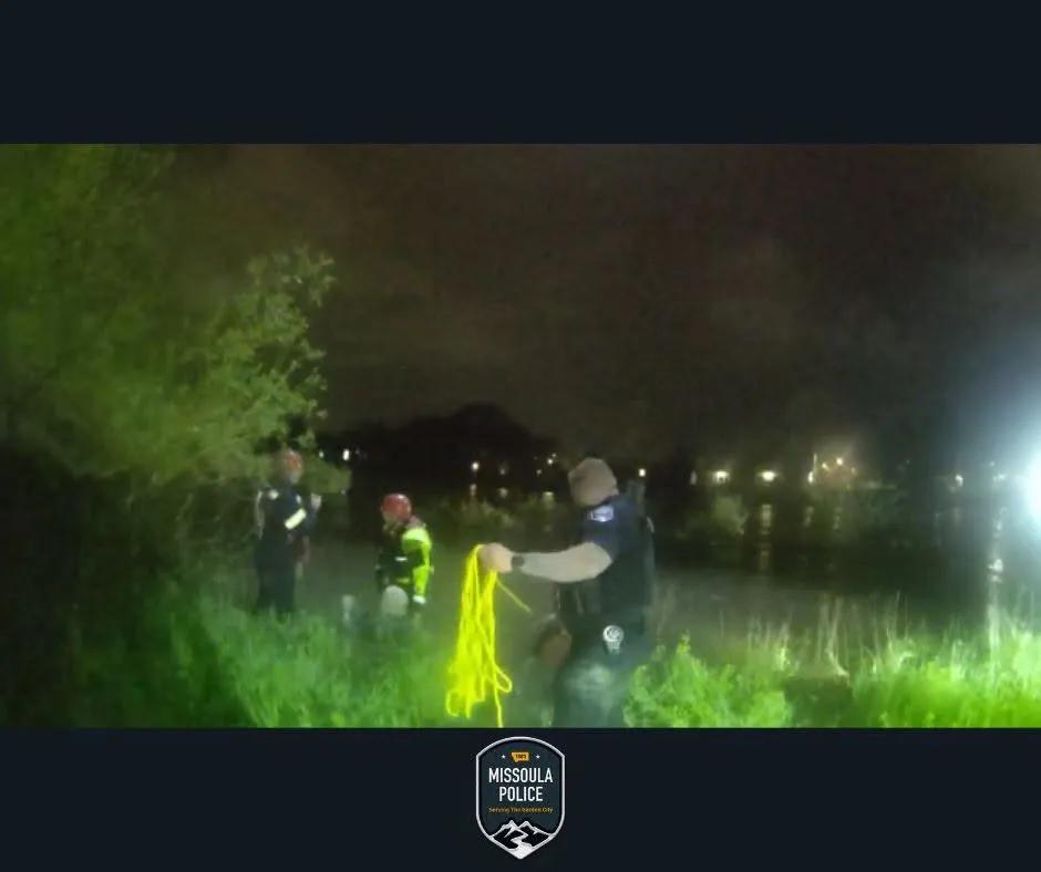 Missoula Police officers holding a bright yellow rescue rope on the dark riverbank at night.