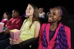 Middle school students smiling and eating popcorn while watching a movie inside a theater.