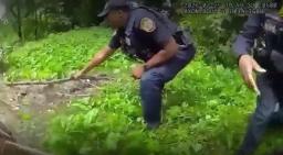 Police officer extending a long stick down a steep grassy embankment during a water rescue call in Memphis, Tennessee.