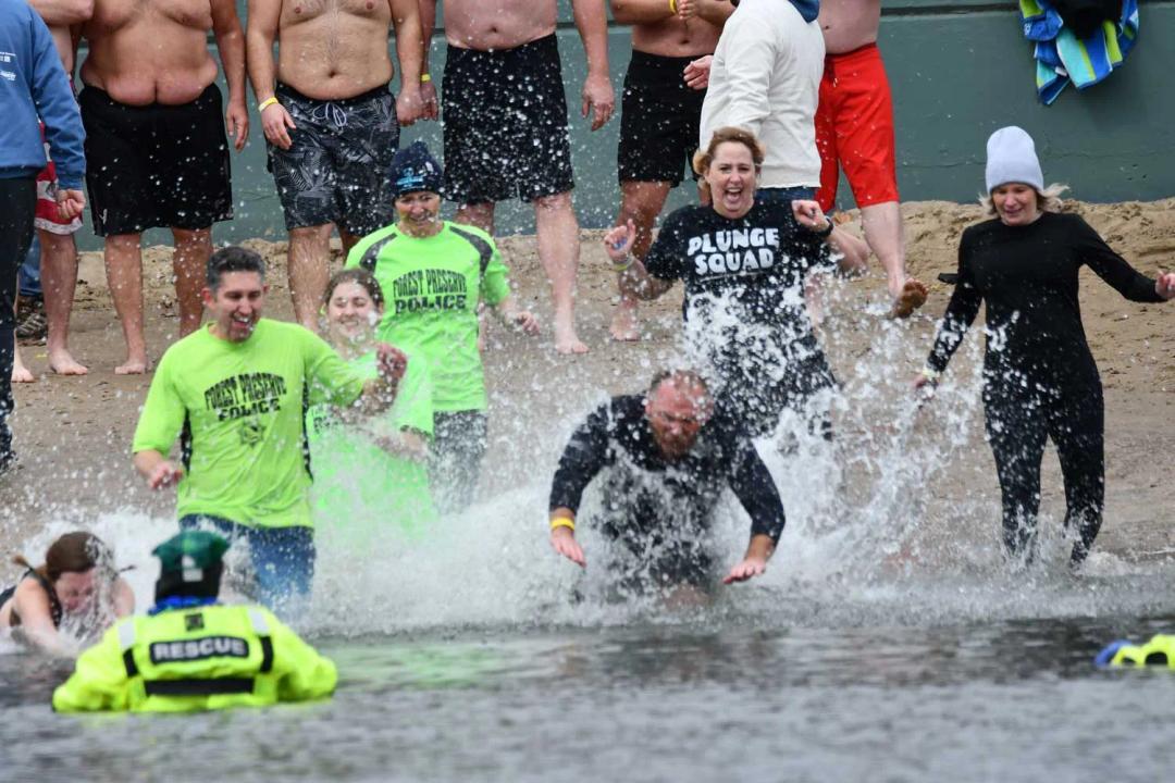 Forest Preserve District police officers and community members run into freezing water at a beach during a polar plunge.