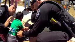 Rialto police officers kneel on a sidewalk assisting a young child during an emergency call.  