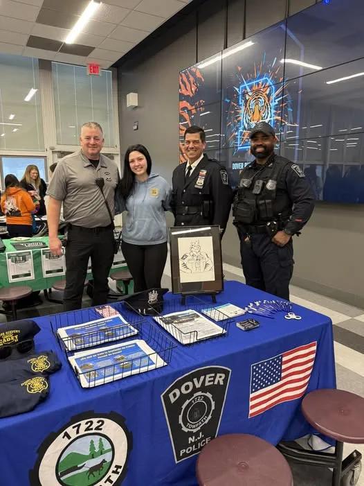 Dover Police Department officers and staff standing behind a recruitment table at a high school career fair.