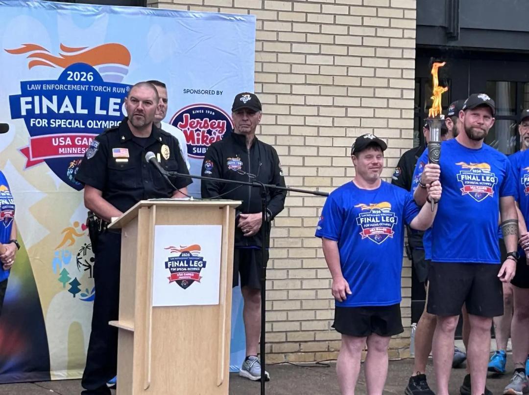 A Special Olympics athlete smiles while holding up the lit Flame of Hope torch alongside an officer in a blue final leg shirt.