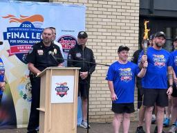 A Special Olympics athlete smiles while holding up the lit Flame of Hope torch alongside an officer in a blue final leg shirt.