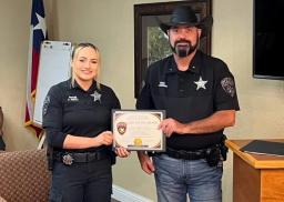 Hughes Springs Police Officer Arron Orrill holding her framed Life-Saving Award certificate presented by Chief Antony Harrison.
