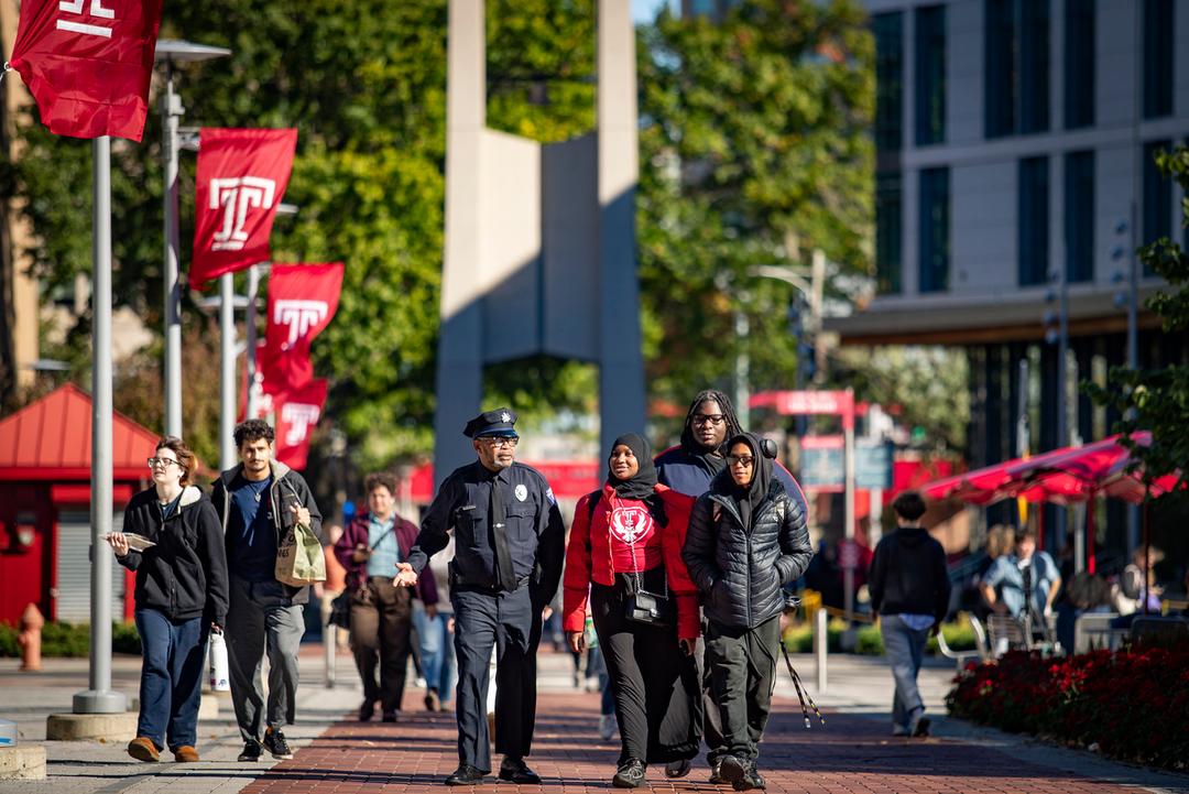 Temple University Police Officer Leroy Wimberly walking on campus pathways with three Carver High School students.