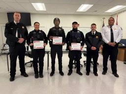 Six uniformed people stand side by side in a room, with three of them holding certificates of appreciation.