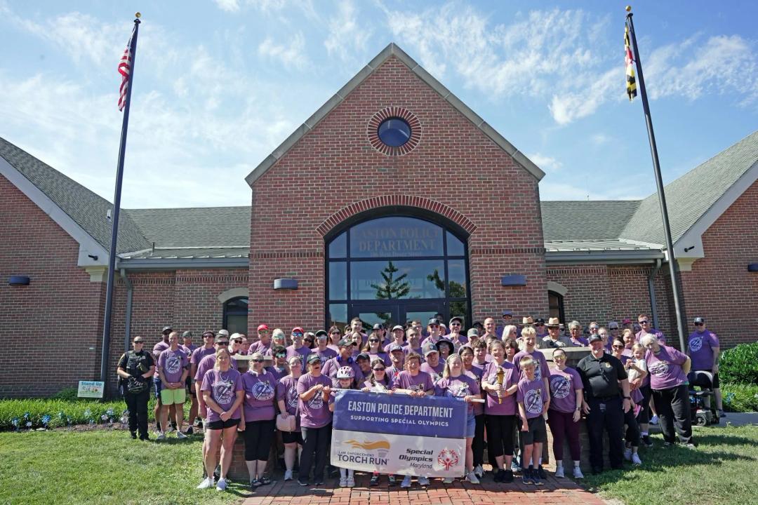 Law enforcement volunteer staff and special athletes posing together with a Special Olympics Maryland torch run banner.