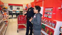 A Raleigh police officer smiling while helping a young boy shop with a red cart at Target.